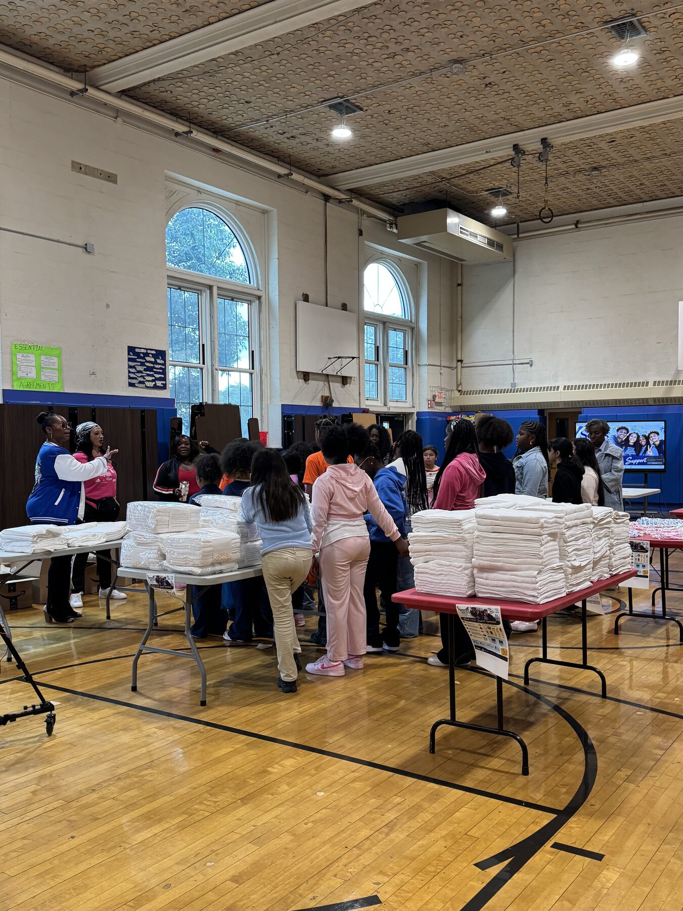 Students and adults organizing stacks of supplies at tables in the Joseph A. McNeil Elementary School gymnasium